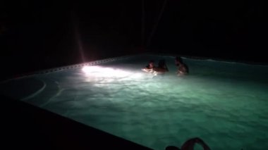 Gece bir havuzda üç arkadaş ve bir kır evindeki bir partide ışıklar.