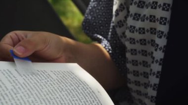 4K 'da bir sayfiye evinde şeffaf bir bölme tutan bir kitap okuyan bir kadının ellerinin yakın çekimi.