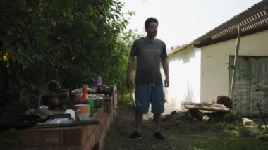 Genç bir beyaz adam barbekü hazırlıyor. Gün içinde yeşillik içinde bir kır evinde dans edip bira içiyor.