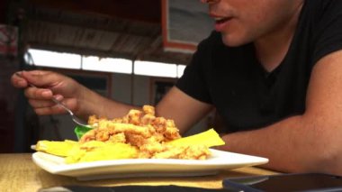 Gün boyunca sahilde bir restoranda kızarmış yukka ile bir tabak balık chicharron yiyen bir adamın yakın çekimi.