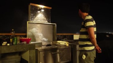 Bir adam gece ızgaranın yanında kömürün ısınmasını beklerken 4K 'daki bir sahil evinde gökyüzüne bakıyor.