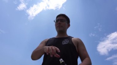 4K 'da güneşli bir günde, elinde viski şişesi ve mavi gökyüzü arkaplanı olan bir adamın yakınından görülüyor.