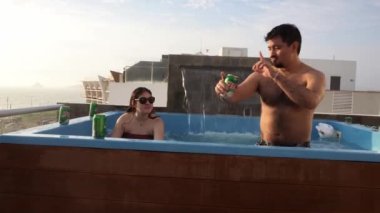 Bir düğün çifti, gün batımında bir plajda havuzda dans edip bira içiyor.