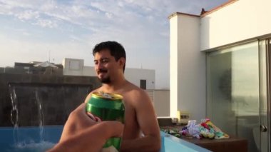 POV, terasta arkadaşlarıyla bir kutu bira kapıp kadeh kaldırıyor. Gün batımlı bir sahil evinde havuzu ve arka planda 4K 'da deniz var.