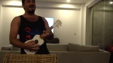 Küçük ukulele gitar çalan bir adam gecenin 4 'ünde arkadaşlarıyla bir sahil evinde mutlu bir şekilde dans ediyor.
