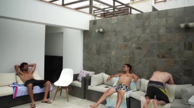 arkadaşlar terasta havlularla koltuklarda oturuyorlar gün içinde havuzda ıslandıktan sonra kurulanıyorlar.