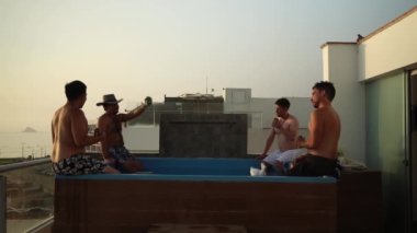 Birkaç arkadaş gün batımında sahile bakan bir evin havuzunda bira kutularıyla gülüp kadeh kaldırıyorlar.