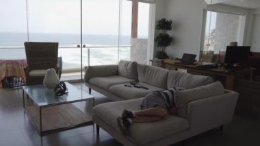 Sahildeki bir evde, arka planda deniz olan bir sandalyede uyuyan bir adam. Gün boyunca 4K 'da.