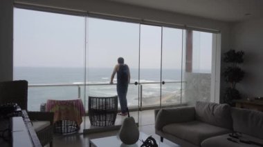 Denize bakan melankolik bir sahil evinin terasında, kafası bulutlu bir günde yere eğilmiş, tanınmayan bir adam.