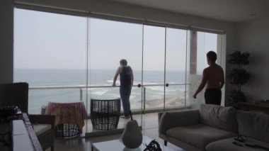 Bulutlu bir günde, sahildeki bir evin terasında denize bakan iki arkadaş.