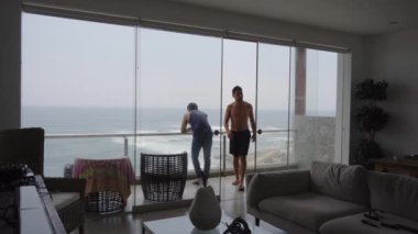 İki arkadaş arka planda deniz olan bir sahil evinden 4K 'da ayrılıyorlar.