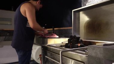 Bir adamın, gecenin 4 'ünde arkadaşlarıyla birlikte bir sahil evinin çatısında alevler içinde yanan altıgen şeklinde kömür yığınıyla ızgaranın yanında et keserken yakın plan çekimi.