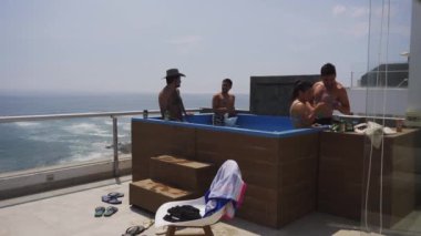 4k 'da güneşli bir günde, arka planda deniz olan bir sahil evinin terasında havuzda bira ve şarap içen birkaç arkadaş Punta Hermosa, Peru - Ocak 2022