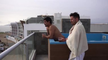 Profil görüntüsü ufka bakan iki arkadaşın gündüz vakti havuzda bira içtiği bir sahil evinin terasında 4K 'da.