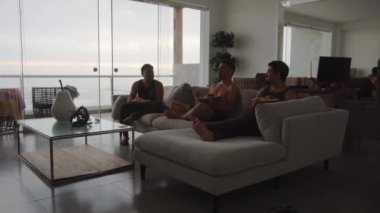Arkadaşların oturma odasında oturup yemek yediği, TV izlediği ve bulutlu bir günde deniz dalgalarının arka planına sahip bir sahil evinde gülüp eğlendiği bir kamera. 4k içinde zaman aşımı
