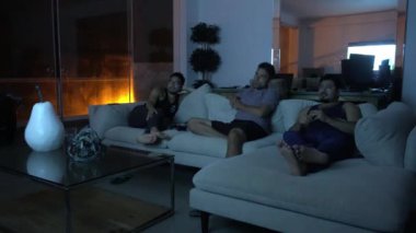 Arkadaşların oturma odasındaki kanepede oturup geceleri deniz dalgalarının arka planına sahip bir sahil evinde televizyon izlediği kısa bir kamera. 4k içinde zaman aşımı