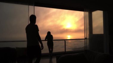 Bir adam, sahil evinin terasında eşine sarılacak. Deniz dalgaları ve 4K 'da uçan martılarla güzel, turuncu bir günbatımı olacak.