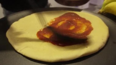 closeup pouring a red sauce on a dough to prepare a homemade pizza in the kitchen