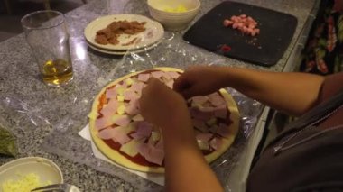 Mutfakta hazırlanmış ev yapımı pizzaya jambon ekliyorum.