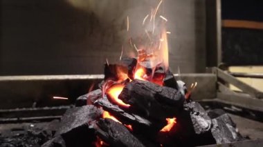 Çok sayıda kömür parçasının alev alev yanması ve kül ve kıvılcımların havada uçuşması gece 4K 'da dumanlı ızgarada.