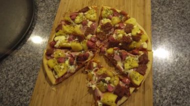 Mutfaktaki ahşap bir tahtadan ev yapımı bir pizzanın üçgen dilimini kapmak için birkaç el yaklaştı.