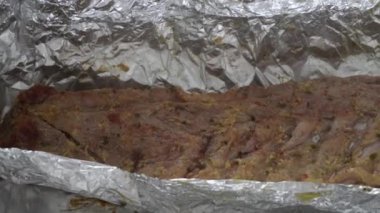 Bir domuz kaburgasını alüminyum folyoyla çevirerek fırından yeni çıkmış maşayla birlikte 4K 'da porselen kutusunda.