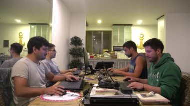 Birkaç arkadaş yemek odasında dizüstü bilgisayarlarıyla oynuyorlar.