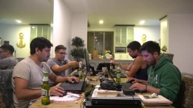 Şafak vakti birkaç arkadaşın laptoplarıyla odada çalışırken arkadaşları ve ortakları onlara bakarken ve tezahürat yaparken çekilmiş bir kamera. zaman aşımı