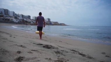 Sahilde sarı muz şeklinde şamandıra çıkaran bir adam Punta Hermosa, Lima, Peru 'daki Senyoritas plajında denizin dalgaları tarafından taşınıyor.