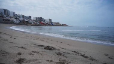 Kum, deniz, dalgalar, binalar ve martılar Punta Hermosa, Lima, Peru 'daki Senyoritas plajlarında görülür.