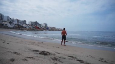 Sırtında polo tişörtü olmayan, kumlu, dalgalı ve cep telefonuna bakan bir adam. Soyutlama, barış, rahatlama kavramı