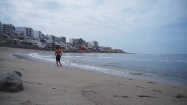 Kum, dalga ve binalarla deniz kıyısında direksiz koşan bir adam.