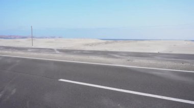 4k 'da, arka planda denizden çöle doğru esen güçlü rüzgârlar yüzünden yol boyunca yer değiştiren kumun yakın çekimi.