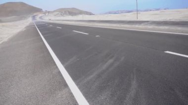 POV, arka planda denizden çöle doğru esen güçlü rüzgar yüzünden yolun her tarafına dağılan kumun yakın çekimini görüyor. Gün boyunca 4K 'lık bir bakış açısıyla.