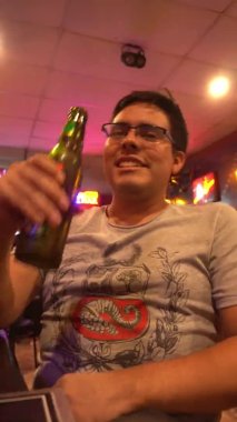 Gece 4K 'de bir barda cam şişeden bira içen bir adamın dikey yakın çekimi.