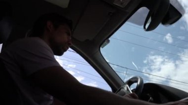 4K 'lık açık ve mavi bir gökyüzü ile gündüz araba süren bir adamın yolcu koltuğunun altında alçak açı görüntüsü.