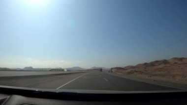 POV arabayı sürüyor. Kumun hareketini görüyor. Gün içindeki güçlü rüzgârın etkisinde.