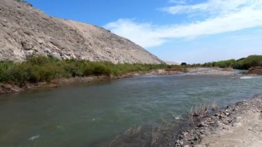 POV nehir ve tepeler arasında açık mavi gökyüzü olan bitki örtüsü arasında tarım arazisi görüyor. Casma 'da, Lima' da, Peru 'da 4K' da bir bakış açısı