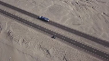 Çölün ortasındaki otobanın hava aracı görüntüsü. Kum, deniz kıyısının güçlü rüzgârıyla hareket ediyor. Gün içinde, 4K 'da, yolun kenarında park etmiş bir kamyonla.