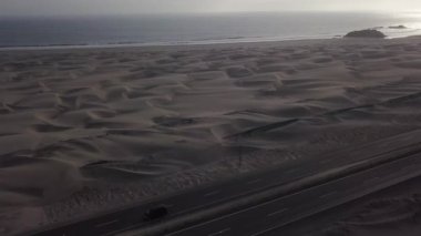 Gökyüzünün güzel hava aracı manzarası, parlak güneş denizin üzerindeki bulutlarla kaplı ve yolun kenarında bakir bir çöl, kamyonlar, arabalar ve motosikletler 4K 'da.