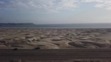 Renkli dağları ve deniz kenarındaki kumulları olan güzel bir çöl manzarası ve arabalı bir yol ve 4K 'da kamyonetinin dışında bir adam.