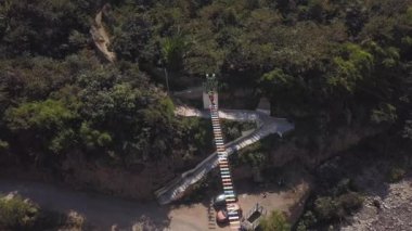 Bir asma köprüden aşağıya bakan insansız hava aracı dağların yamaçlarında farklı renkli bir nehirde yürüyen insanlar ve kuş bakışı yeşil ağaçlar.