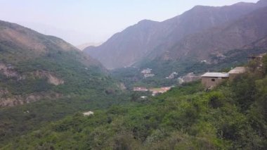 4k 'da, San Mateo de Otao dağlarındaki bir köyde dağların, yeşil ağaçların ve evlerin arasından geçen bir teleferik görüntüsü.