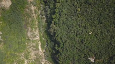 Beyaz bir teleferiğin hava aracı görüntüsü bir sürü bitki örtüsü ve dağların arasında bir nehir dağların arasında gün içinde yeşil ağaçların olduğu bir kuş bakışı 4K 'ya bakıyor.