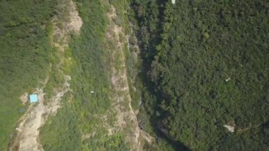 Beyaz bir teleferiğin hava aracı görüntüsü bir sürü bitki örtüsü ve dağların arasında bir nehir dağların arasında gün içinde yeşil ağaçların olduğu bir kuş bakışı 4K 'ya bakıyor.