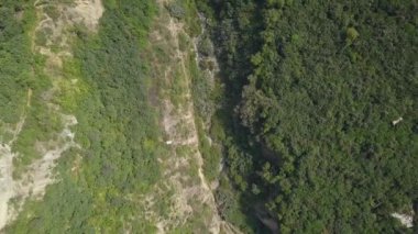 Beyaz bir teleferiğin hava aracı görüntüsü bir sürü bitki örtüsü ve dağların arasında bir nehir dağların arasında gün içinde yeşil ağaçların olduğu bir kuş bakışı 4K 'ya bakıyor.