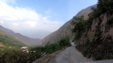 Arabadaki POV dağlık bölgelerdeki patika yolu boyunca ilerliyor ve gün içinde yeşil ağaçlar görülebiliyor.