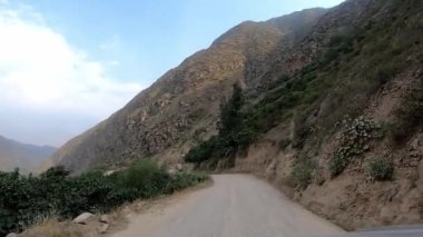 Arabadaki POV dağlık bölgelerdeki patika yolu boyunca ilerliyor ve gün içinde yeşil ağaçlar görülebiliyor.