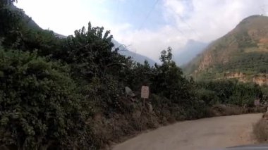 Arabadaki POV dağlık bölgelerdeki patika yolu boyunca ilerliyor. Yüksek voltaj kabloları ve antenleri olan yeşil ağaçlar.