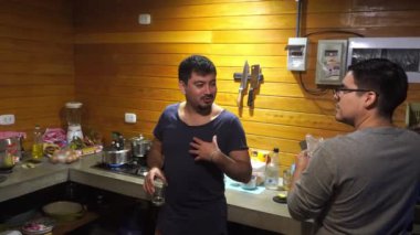 Birkaç arkadaş mutfakta içki içip kameraya bakıyor, konuşuyor ve gülümsüyor.